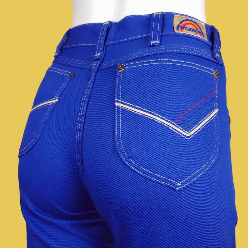 May include: A pair of blue denim jeans with white stitching and a contrasting white pocket. The jeans have a Wrangler logo on the back pocket.