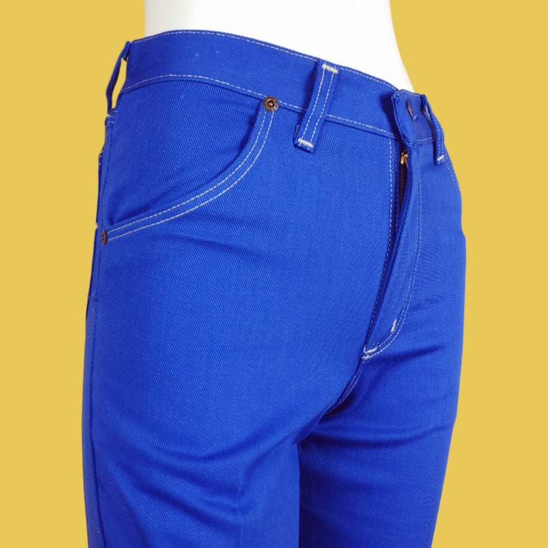 May include: A pair of blue denim jeans with white stitching. The jeans have a zip fly and a button fastening.