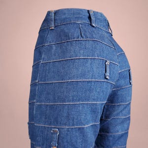 K&ouml;nnte beinhalten: Blaue Jeans mit horizontalen Nahtdetails. Die Jeans haben ein klassisches F&uuml;nf-Taschen-Design und einen Knopf- und Rei&szlig;verschluss. Die Jeans sind aus mittelblauem Denim.