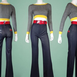 May include: A three-piece outfit comprising a black and white polka dot long-sleeved crop top with yellow trim, a red belt, and dark blue flared jeans. The jeans have embroidered designs on the back pockets. The outfit is displayed on a mannequin.