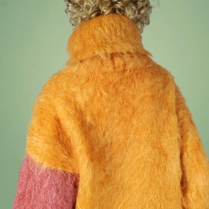 May include: A fuzzy, two-toned sweater with a high neck. The sweater is mostly orange with a pink section on one sleeve.