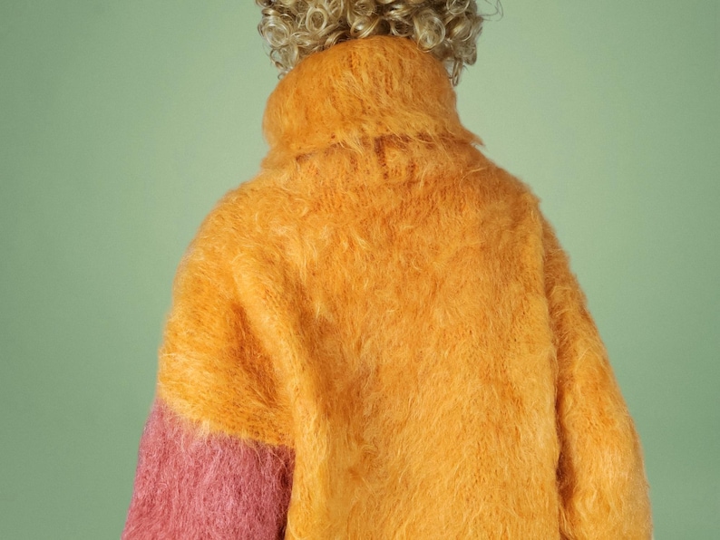 May include: A fuzzy, two-toned sweater with a high neck. The sweater is mostly orange with a pink section on one sleeve.