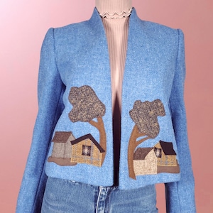 May include: A light blue cropped jacket with a unique design featuring two brown trees and houses appliqued on the front.