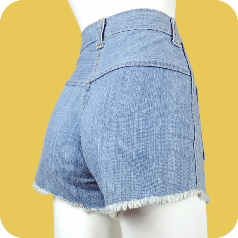 K&ouml;nnte beinhalten: Hellblaue Jeans-Shorts mit ausgefranstem Saum. Die Shorts haben eine hohe Taille und einen Knopfverschluss.