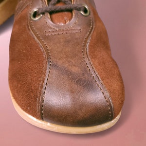 May include: Close-up of a brown leather and suede shoe with a stitched seam. The shoe has a cream-colored sole.