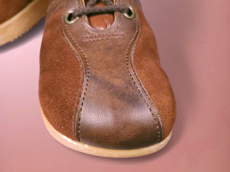 May include: Close-up of a brown leather and suede shoe with a stitched seam. The shoe has a cream-colored sole.
