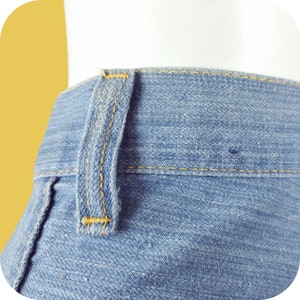 K&ouml;nnte beinhalten: Nahaufnahme einer blauen Jeanshose mit gelber Steppnaht. Die Jeans hat eine einzelne G&uuml;rtelschlaufe am Bund.