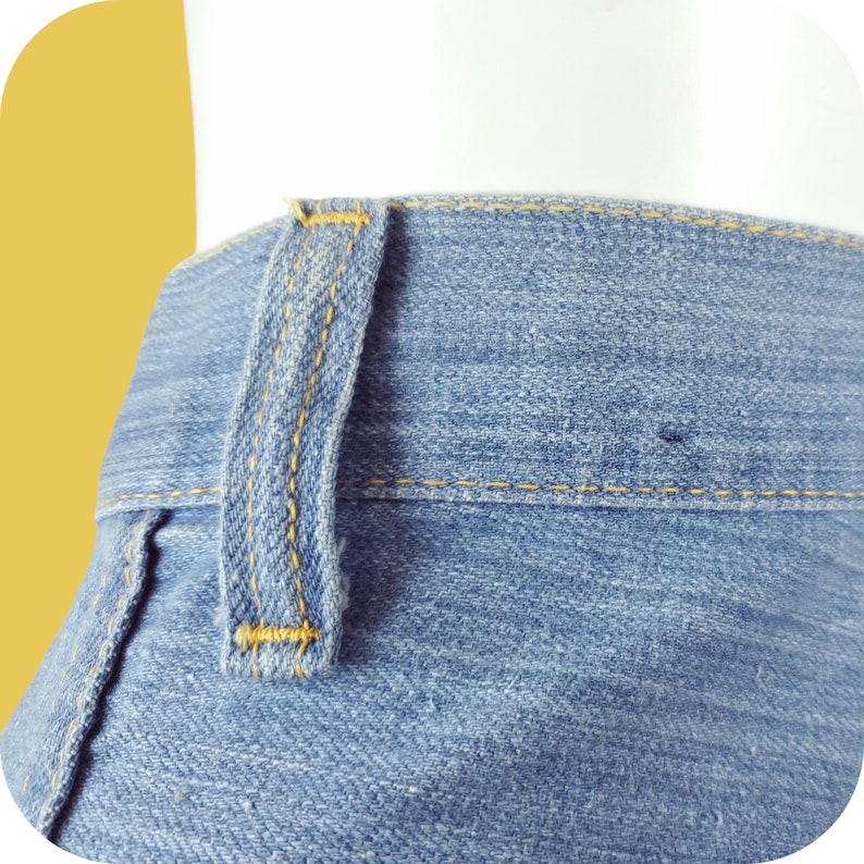 K&ouml;nnte beinhalten: Nahaufnahme einer blauen Jeanshose mit gelber Steppnaht. Die Jeans hat eine einzelne G&uuml;rtelschlaufe am Bund.