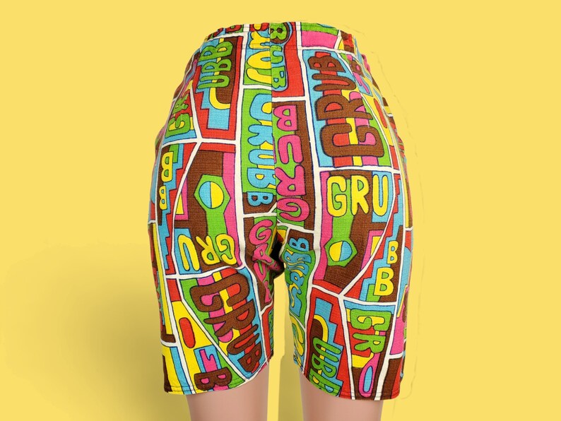 Peut inclure: Shorts color&eacute;s avec un motif g&eacute;om&eacute;trique marron, rouge, rose, jaune, vert et bleu. Les shorts pr&eacute;sentent le mot "GRUB" et d'autres textes dans le design. Les shorts sont pr&eacute;sent&eacute;s sur un fond jaune.
