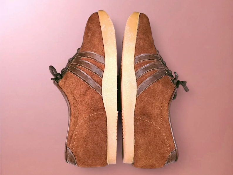 May include: A pair of brown suede sneakers with white soles and brown laces. The sneakers have a classic design with three brown stripes on each side.