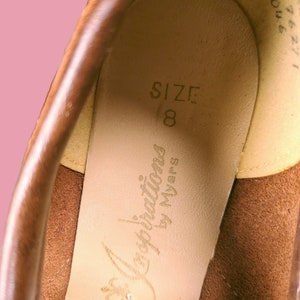 May include: Close-up of the inside of a brown leather shoe. The insole is beige and has the text "Inspirations by Myers" and "SIZE 8" printed on it.
