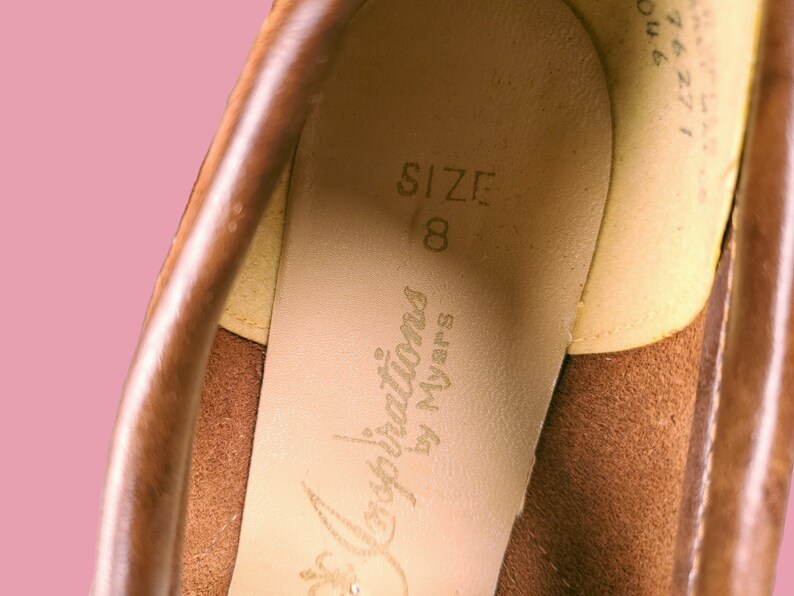 May include: Close-up of the inside of a brown leather shoe. The insole is beige and has the text "Inspirations by Myers" and "SIZE 8" printed on it.