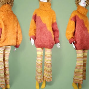 May include: A fuzzy, two-toned sweater with a high neck and long sleeves. The sweater is orange and pink with a color block design. The sweater is worn with striped pants.