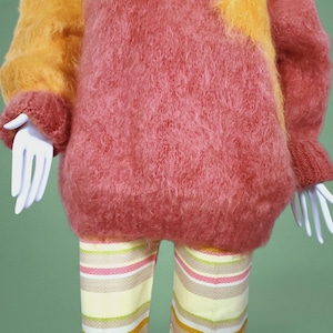 May include: A fuzzy pink and orange sweater with long sleeves and a loose fit. The sweater is made of a soft, fluffy material.
