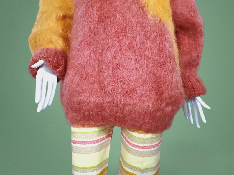 May include: A fuzzy pink and orange sweater with long sleeves and a loose fit. The sweater is made of a soft, fluffy material.