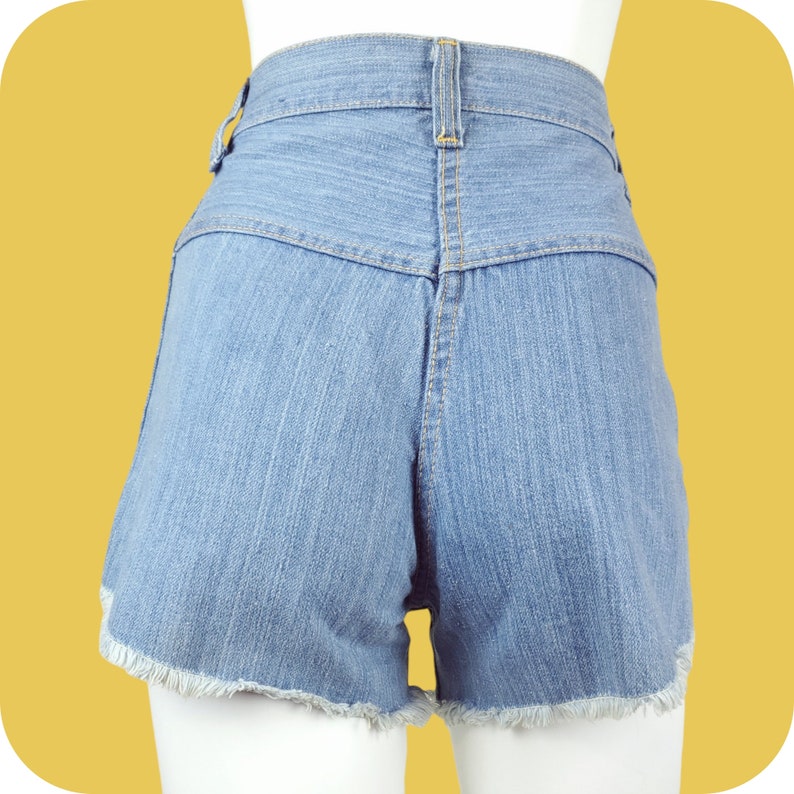 K&ouml;nnte beinhalten: Hellblaue Jeans-Shorts mit ausgefranstem Saum. Die Shorts haben eine hohe Taille und einen Knopfverschluss.