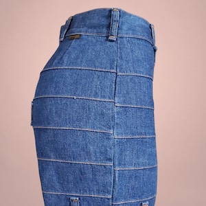 K&ouml;nnte beinhalten: Ein blauer Jeansrock mit horizontalen Bahnen. Der Rock hat ein klassisches F&uuml;nf-Taschen-Design und einen Bund mit G&uuml;rtelschlaufen. Der Denim hat eine mittlere Waschung und der Rock scheint eine Midi-L&auml;nge zu haben.