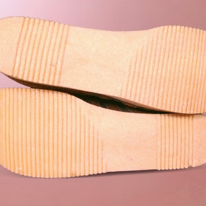 May include: Close-up of the bottom of a pair of brown leather shoes with a textured sole.