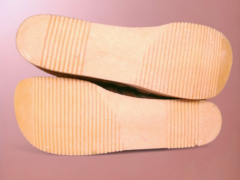 May include: Close-up of the bottom of a pair of brown leather shoes with a textured sole.