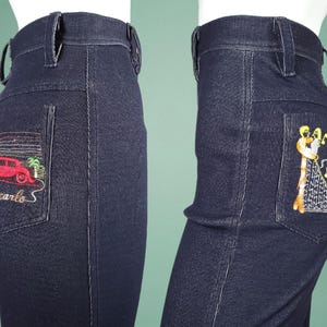 May include: Dark blue denim jeans with embroidered designs on the back pockets. One pocket features a red car and the text "Montecarlo S". The other pocket has an embroidered image of two figures dancing with musical notes.