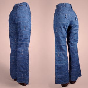 K&ouml;nnte beinhalten: Zwei Ansichten einer blauen Jeanshose mit horizontalen wei&szlig;en N&auml;hten und rechteckigen Akzenten. Die Hose hat eine hohe Taille und ein ausgestelltes Bein. Der Denim hat eine mittlere Waschung, und die N&auml;hte erzeugen einen gestreiften Effekt.