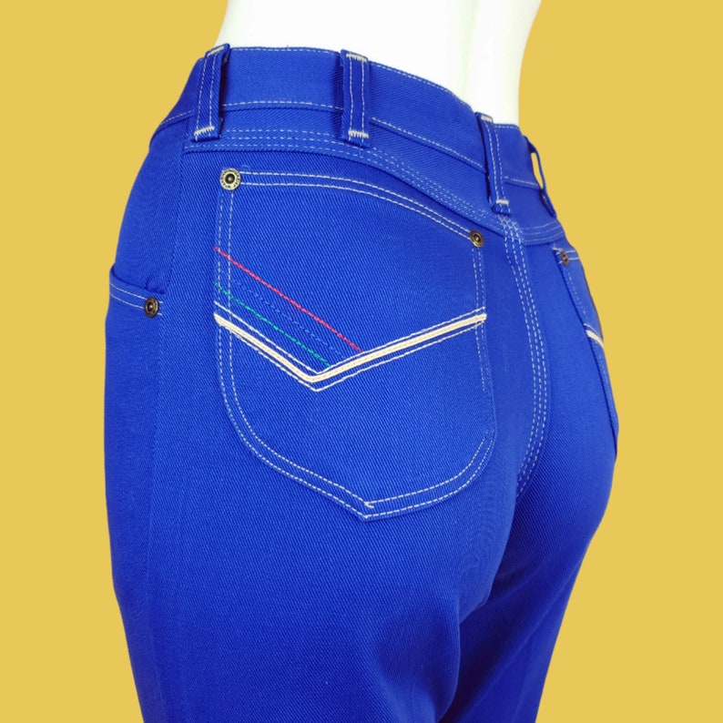 May include: Blue denim jeans with a white stitched back pocket and colourful stitching detail.