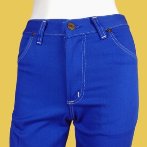 May include: A pair of blue denim jeans with white stitching. The jeans have a button fly and a small brown leather patch with the word "Wrangler" on the back.