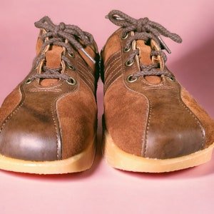 May include: A pair of brown suede sneakers with laces. The sneakers have a light brown sole and a dark brown leather toe.