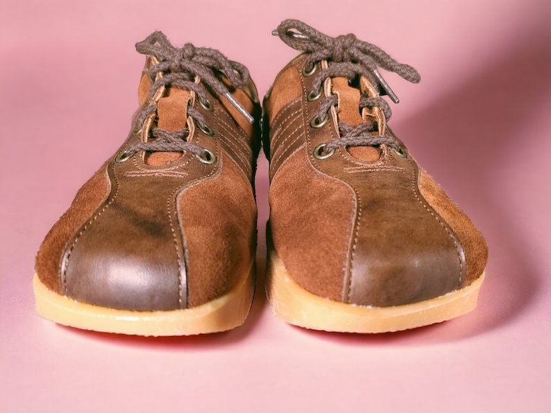 May include: A pair of brown suede sneakers with laces. The sneakers have a light brown sole and a dark brown leather toe.