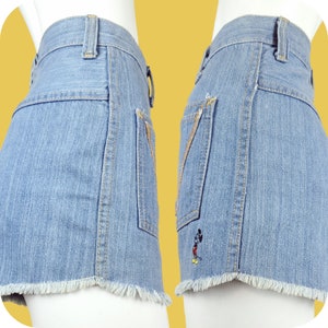 K&ouml;nnte beinhalten: Hellblaue Jeans-Shorts mit ausgefranstem Saum und einer Mickey-Mouse-Stickerei auf der Ges&auml;&szlig;tasche.