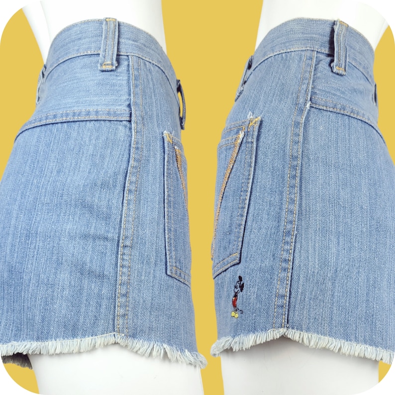 K&ouml;nnte beinhalten: Hellblaue Jeans-Shorts mit ausgefranstem Saum und einer Mickey-Mouse-Stickerei auf der Ges&auml;&szlig;tasche.