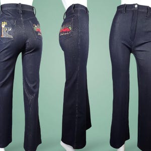 May include: Dark blue denim bell-bottom jeans. The back pockets feature colourful embroidered designs. The jeans have a high waist and a flared leg. The jeans are displayed on a mannequin. The jeans are a vintage style.