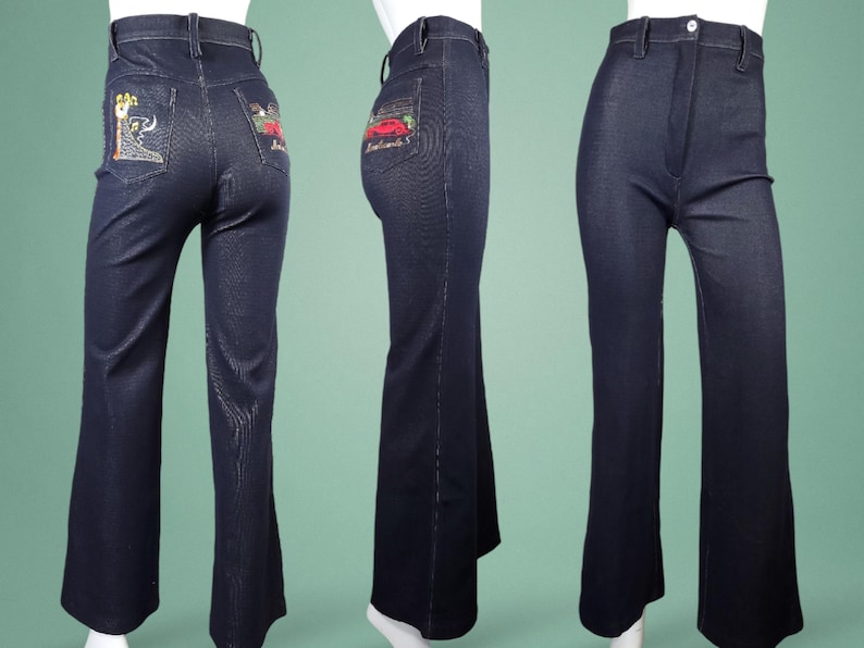 May include: Dark blue denim bell-bottom jeans. The back pockets feature colourful embroidered designs. The jeans have a high waist and a flared leg. The jeans are displayed on a mannequin. The jeans are a vintage style.