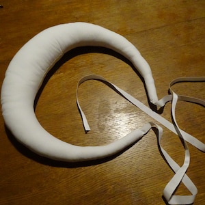 Könnte beinhalten: Ein weißes Stoff-Haarband mit einer gebogenen Form und weißen Schleifenbändern.