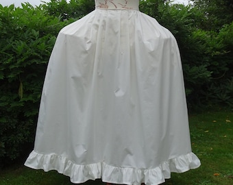 May include: A white, ruffled apron with a wide skirt. The apron is made of a smooth, opaque fabric and has a decorative ruffle along the bottom hem. The apron's waistband features a floral pattern. The apron is displayed outdoors.