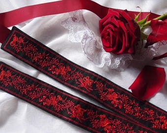 Puede incluir: Dos cintas negras bordadas con diseños florales rojos se muestran sobre una superficie blanca, junto a una rosa roja y una cinta roja. Las cintas presentan intrincados bordados rojos de rosas y vides.