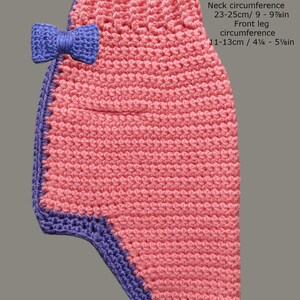 May include: Pink crocheted dog sweater with a purple trim and a purple bow. Length from neck to tail: 22 cm / 8 5/8 in. Chest circumference: 31-33 cm / 12 1/8 - 13 in. Neck circumference: 23-25 cm / 9 - 9 7/8 in. Front leg circumference: 11-13 cm / 4 1/4 - 5 1/8 in.
