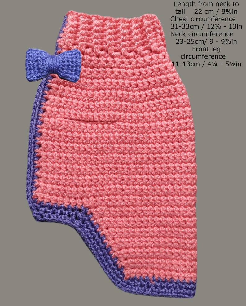 May include: Pink crocheted dog sweater with a purple trim and a purple bow. Length from neck to tail: 22 cm / 8 5/8 in. Chest circumference: 31-33 cm / 12 1/8 - 13 in. Neck circumference: 23-25 cm / 9 - 9 7/8 in. Front leg circumference: 11-13 cm / 4 1/4 - 5 1/8 in.