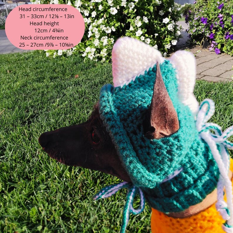 May include: A black dog wearing a teal and white crocheted hat with cat ears. The hat has a white ribbon tied under the chin. The dog is wearing a yellow shirt. The hat has measurements in inches and centimeters.