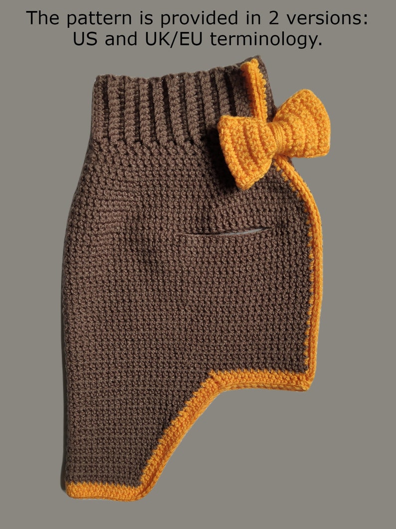 May include: A brown crocheted dog sweater with a yellow crocheted bow on the shoulder. The sweater has a yellow trim around the edges.