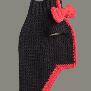 May include: Black crocheted dog sweater with a red crocheted bow. The sweater has a red trim around the edges.