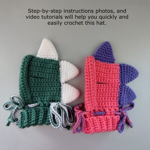 May include: Two crocheted dinosaur hats, one green and white, the other pink and purple. Both hats have a small hole for the eyes and are tied with matching colored strings.