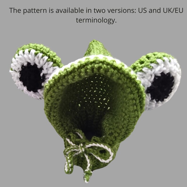 May include: Green crocheted frog hat with white and black accents. The hat has a pointed top and two large ears. The hat is tied at the bottom with a white and green ribbon.
