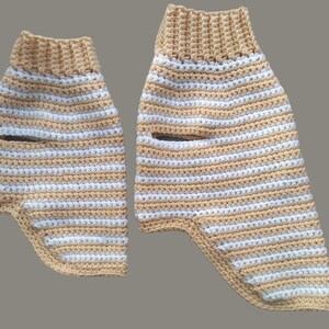 May include: Two crocheted striped leg warmers in beige and white. The leg warmers are made with a chunky yarn and have a simple design.