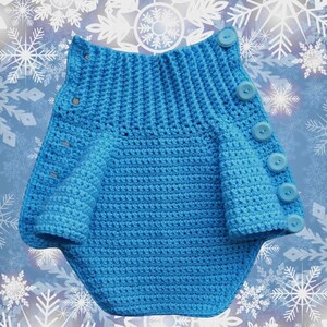 May include: A blue crocheted baby romper with a button closure. The romper has a ruffled hem and is made with a soft, textured yarn.