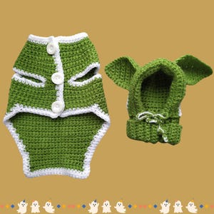 May include: Green crocheted dog costume with a white trim. The costume includes a hooded jacket and a vest.