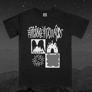 May include: Black t-shirt with a white graphic design. The design includes the text "FOOSOKE FICKIMATOS" above four squares. The squares contain images of angel wings, a castle, a starburst, and a bear. The text "YOU ARE THE ONLY ONE" is below the angel wings.