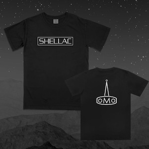 May include: Black t-shirts with white text. One shirt displays "SHELLAC" in a rectangular box. The other shirt shows a white graphic on the back. The background features a starry sky and a mountain range.