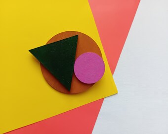 Könnte beinhalten: Ein grünes Dreieck, ein rosa Kreis und ein brauner Kreis auf einem gelben, rosa und weißen Hintergrund.