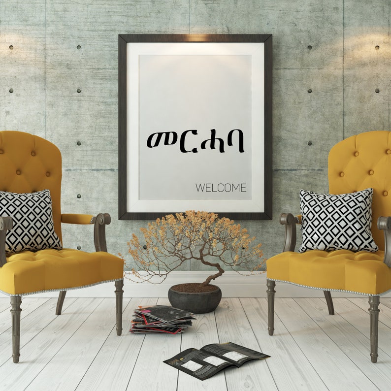 May include: Two yellow chairs with black and white patterned pillows sit in front of a framed print with the text "Welcome" and the Amharic word for "Welcome" in black lettering. A small bonsai tree sits on the floor in front of the chairs.